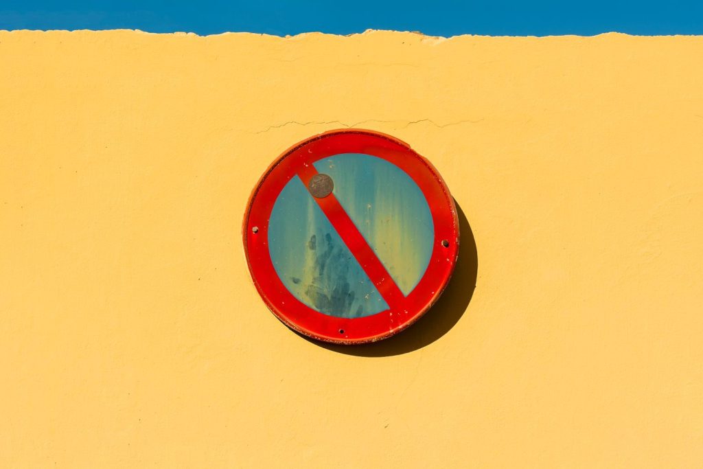 A minimalist red no entry sign on a vibrant yellow wall under a blue sky.